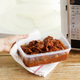 hand holding tupperware full of food in front of microwave